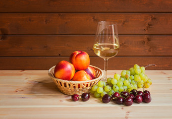 Glass of white wine and fresh ripe fruits on wooden table.