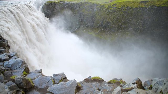 Icelandic Dettifoss waterfall closeup in Iceland gray water mist and rocky cliff spraying and people standing far on overlook