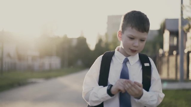 CU, Tracking: Portrait of schoolboy, with knapsack behind his back, in school uniform. He goes on the road from school and counts on his fingers, he thinks.