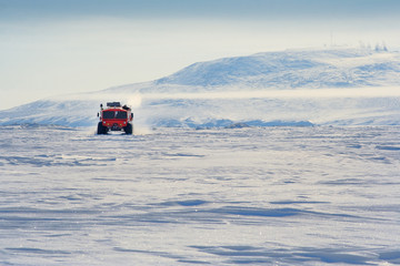 The all-terrain vehicle on tires of ultralow pressure goes on ice. Travels in the Arctic, Extreme North. In the distance, the hill is covered with snow. Chukotka, Siberia, Far East of Russia.