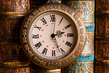 Obraz na płótnie Canvas Antique clock on the background of vintage books. Mechanical clockwork on a chain.