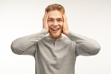 Emotional stupefied male with happy look, receives gift from boyfriend, expresses surprise and astonishment, has light hair, isolated over white background in studio   