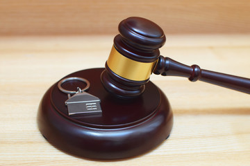 Hardwood gavel laying on sound block next to metallic key ring in shape of house. Concept of real estate auction or law.