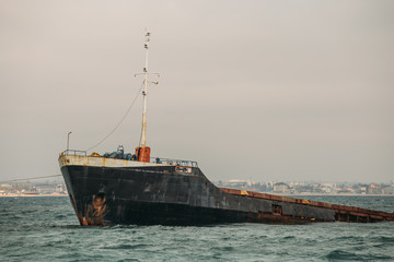 Fototapeta premium Sunken ship near seaside. Shipwreck vessel with nose of ship above sea water