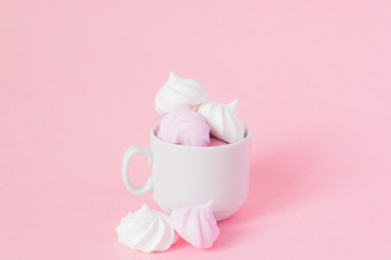 White and pink twisted meringues in a small porcelain coffe cup on pink background. French dessert prepared from whipped with sugar and baked egg whites. Greeting card with copy space