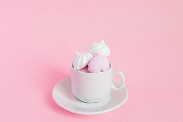 Fototapeta na wymiar White and pink twisted meringues in a small porcelain coffe cup on pink background. French dessert prepared from whipped with sugar and baked egg whites. Greeting card with copy space