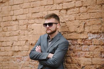 A man with a beard and sunglasses in a gray suit poses on the street to advertise men's clothing. Advertising menswear