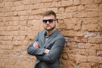 Obraz premium A man with a beard and sunglasses in a gray suit poses on the street to advertise men's clothing. Advertising menswear