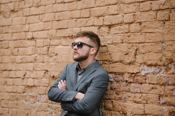 Obraz premium A man with a beard and sunglasses in a gray suit poses on the street to advertise men's clothing. Advertising menswear