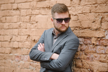 Obraz premium A man with a beard and sunglasses in a gray suit poses on the street to advertise men's clothing. Advertising menswear