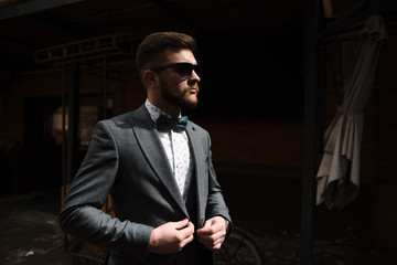 A man with a beard and sunglasses in a gray suit poses on the street to advertise men's clothing. Advertising menswear