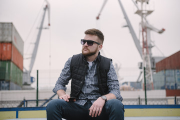 A man with a beard and sunglasses in a plaid shirt and waistcoat posing on the street to advertise...