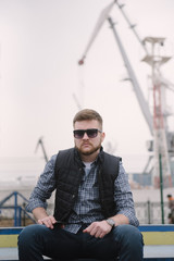A man with a beard and sunglasses in a plaid shirt and waistcoat posing on the street to advertise...
