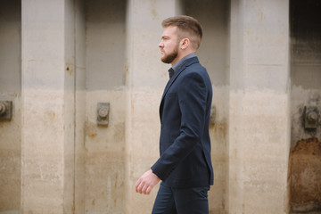 Obraz premium A man with a beard in a blue suit poses on the street to advertise men's clothing. Advertising menswear