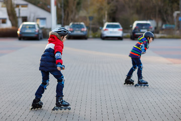 Two little kids boys skating with rollers in the city. Happy children, siblings and best friends in...