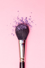 Makeup brush and pink eye shadow on pink background. Vertical