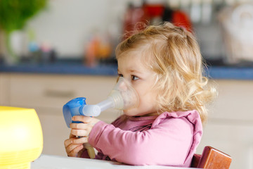 Little toddler girl making inhalation with nebulizer at home. Father or mother helping and holding...