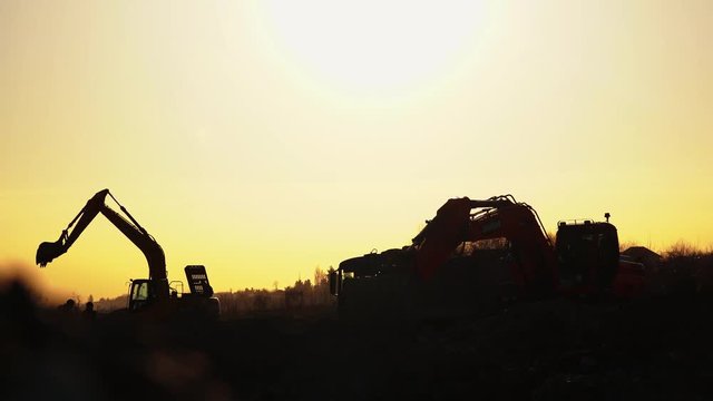 Construction Video At construction site The silhouette excavator is digging ground and lifting a large mortar with engineering and construction workers to help with colorful sunset