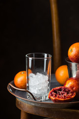 Empty glass for blood orange juice with ice and orange fruits on dark background
