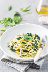 Spaghetti pasta with spinach and green pesto, in a white plate on gray stone background