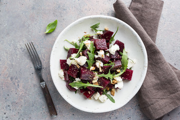beetroot salad with blue cheese, arugula and walnut in a white plate on gray background, top view