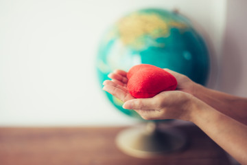 Close up of woman hands holding red heart over blurred world globe on wooden table , christian mission and peaceful concept, earth day background. Copy space