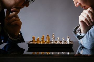 Two unrecogniazble businessmen thinking over moves while playing chess against gray background