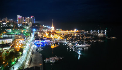 Sochi sea port. Aerial drone. Berth for marine yachts and boats. The historic building of the seaport. Evening illumination of the city.
