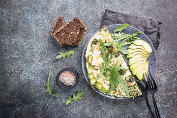 Omelette with avocado and arugula on gray ceramic plate on stone background, top view. Healthy breakfast.