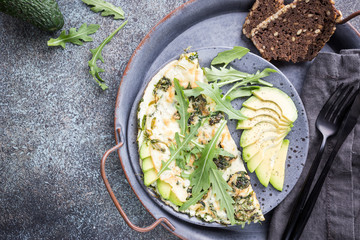 Omelette with avocado and arugula on gray ceramic plate on stone background, top view. Healthy breakfast.