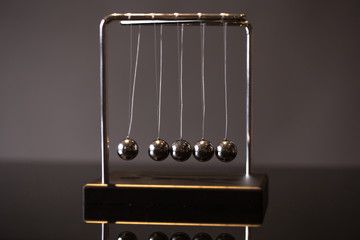 Closeup metal Newton cradle placed on gray background as representation of momentum concept