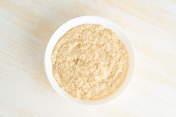 Oatmeal, large bowl of tasty healthy porridge for breakfast, morning meal. Top view, close up, white wooden rustic table. Vegan diet