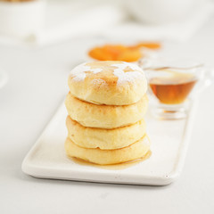Fried cheese cakes, sweet cheese pancakes on white plate on white background. Home tea party
