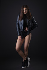Brunette girl in a black leather jacket . Beautiful model on a dark background. Full-length studio photosession