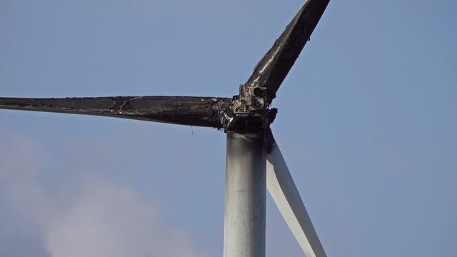 Burned damaged wind turbine against blue sky, 4k