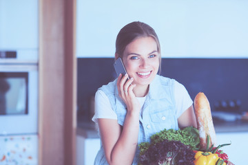Smiling woman with mobile phone holding shopping bag in kitchen
