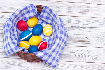 beautiful basket with colored dyed chicken eggs on colorful checkered fabric and on white wooden background, copy space, decorative