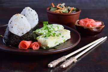 Mix of Japanese food - rice balls onigiri, omelette, pickled ginger, sunomono wakame cucumber salad and chopsticks. Asian breakfast or lunch background