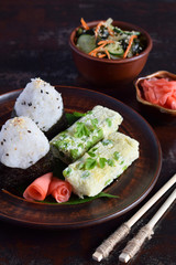 Mix of Japanese food - rice balls onigiri, omelette, pickled ginger, sunomono wakame cucumber salad and chopsticks. Asian breakfast or lunch background