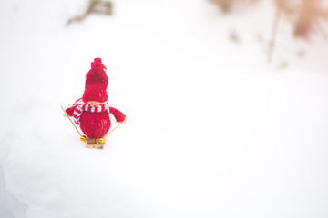 Winter photo with Christmas decorations for pine tree. Knitted snowman toy girl standing on the ski in the forest. Happy holidays ornaments postcard. Snowy weather.