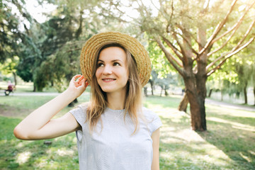 Stylish hipster girl with a straw hat  is standing outdoors. Happy woman in blue dress.  Travel holiday concept. Summer lifestyle photo. Shades of sun and trees.