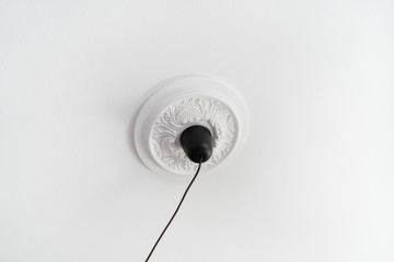 White classical ceiling medallion or rosetta with black cord from light fixture made of paintable polyurethane foam or styrofoam to glue up, easy DIY interior design home decoration project - obrazy, fototapety, plakaty