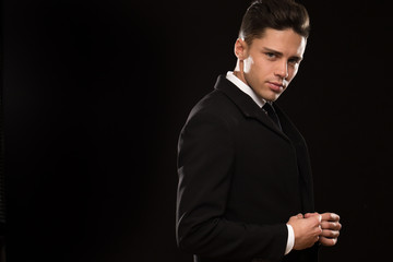 Handsome sexy young man in a classy elegant black suit looking to the camera adjusting his jacket on black background copyspace sexuality seduction macho elegance businessman style