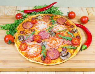 Pizza with sausages and mushrooms on cutting board among vegetables