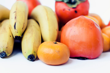 A selection of arranged different fresh fruits of bananas, mandarins, persimmons and lemons on white background close up.