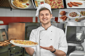 Happy chef showing traditional italian pizza in cafe.