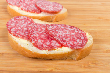 Open sandwiches with salami on bamboo cutting board close-up