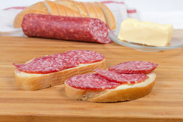 Open sandwiches with salami on bamboo cutting board agains ingredients