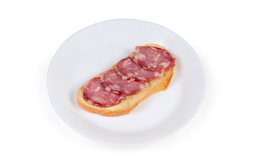 Open sandwich with dry-cured sausage on white dish