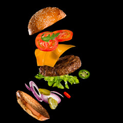 Tasty hamburger with flying ingredients on dark background. High resolution image.